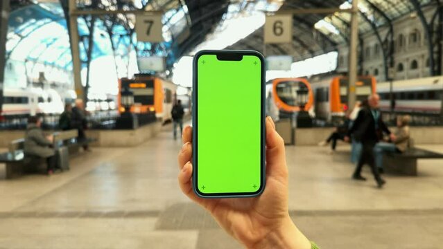 Hand with green screen smartphone in the metro or train station. Hand holding phone with vertical green screen. Traveller in a terminal.