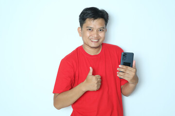 Young Asian man smiling and give thumb up while holding mobile phone. Wearing red a shirt