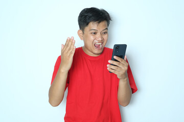 Young Asian man looking to his mobile phone with wow expression. Wearing red a shirt