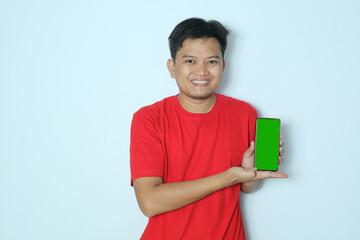 Young Asian man smiles happily while showing the green screen of his cell phone with his open right...