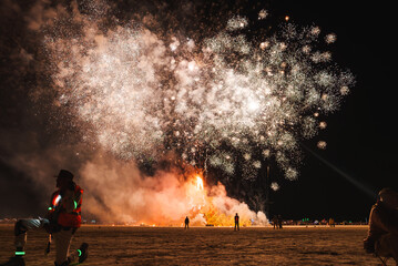 Experience a captivating moment at a nighttime desert event, possibly a music and art festival. Witness a fiery display amidst a diverse crowd under the dark sky.