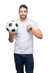 Young man holding soccer football ball over isolated background with surprise face pointing finger to himself