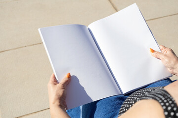 unrecognizable woman holding blank magazine for mockup design, sitting by the swimming pool