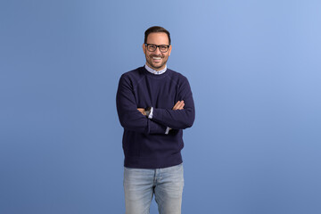 Portrait of handsome CEO with arms crossed and in eyeglasses smiling and posing on blue background