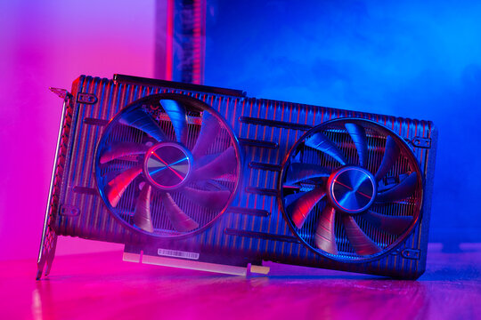 Powerful modern GPU Video Card with two fans with PC case on background in neon light. Rendering and gaming computer hardware components.