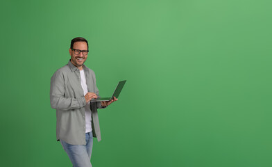 Successful happy male manager working over laptop while standing confidently on green background
