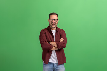 Portrait of happy handsome professional with arms crossed and in glasses posing on green background