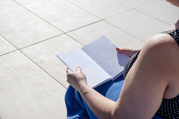 unrecognizable woman holding blank book for mockup design, sitting by the swimming pool