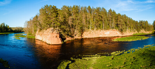panoramic view of the red cliffs along the riverbank in latvia with lush forest and vibrant water
