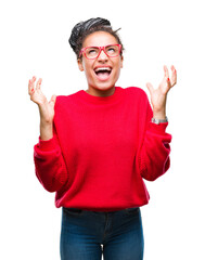 Naklejka premium Young braided hair african american girl wearing sweater and glasses over isolated background celebrating mad and crazy for success with arms raised and closed eyes screaming excited. Winner concept