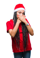 Young braided hair african american girl wearing christmas hat over isolated background shocked covering mouth with hands for mistake. Secret concept.