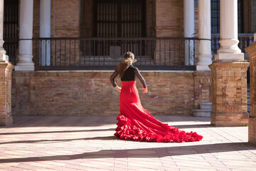 Young, beautiful, brunette woman in black shirt and red skirt, dancing flamenco between marble columns in Spain square in Seville. Flamenco concept, dance, art, typical Spanish.