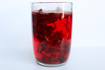 Wedang Uwuh, or traditional tea from brewed sappanwood, ginger, lemongrass and cardamom. In transparent glass, isolated on white background