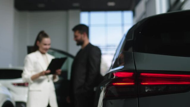 The buyer, a client of a modern car dealership, chooses a car. A dealer talks about a new model of a modern electric car. The concept of test drive, buying an electric car or renting it.