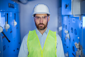 Portrait of serious confident young Caucasian engineer worker with beard in protective goggles in...