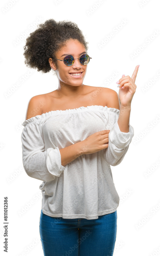 Poster Young afro american woman wearing sunglasses over isolated background with a big smile on face, pointing with hand and finger to the side looking at the camera.