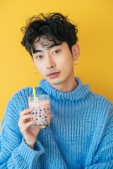 Korean young guy in a blue sweater and with a bubble tee in his hands on a yellow background