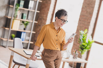 Photo of nice senior woman hold telephone dressed yellow formalwear executive business leader work in cozy beautiful office interior