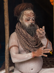 Portrait of an holy male naga sadhu baba with ash on his and long hairs wearning rudraksha necklace during the kumbh festival in India.