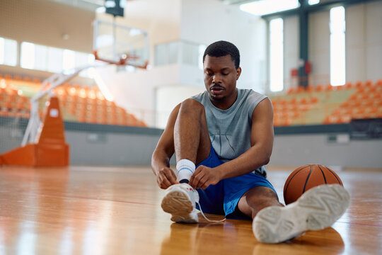 Black athlete tying shoelace during basketball sports training.