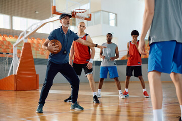 Basketball coach having sports training with group of players in school gymnasium.