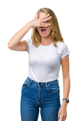 Beautiful young woman wearing casual white t-shirt over isolated background peeking in shock covering face and eyes with hand, looking through fingers with embarrassed expression.