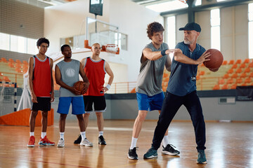 Basketball team having sports training with their coach in school gymnasium.