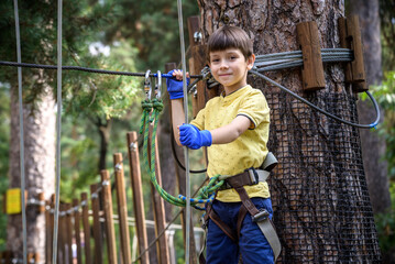 Strong excited young boy playing outdoors in rope park. Caucasian child dressed in casual clothes and sneakers at warm sunny day. Active leisure time with children concept