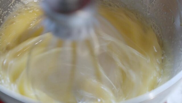 Close-up mixing egg and sugar in a metal bowl with electric kichen mixer. 4k slow motion 100fps video.