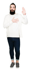 Young hipster man with long hair and beard wearing sporty sweatshirt Swearing with hand on chest...