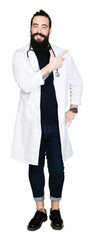 Doctor with long hair wearing medical coat and stethoscope cheerful with a smile of face pointing with hand and finger up to the side with happy and natural expression on face