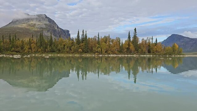 Crossing Lake L&aring;jt&aacute;vrre by boat from the south shore to the north as part of the King's hiking Trail with a view of Sarek National Park and its highest peak Skierfe in early autumn and colorful leaves