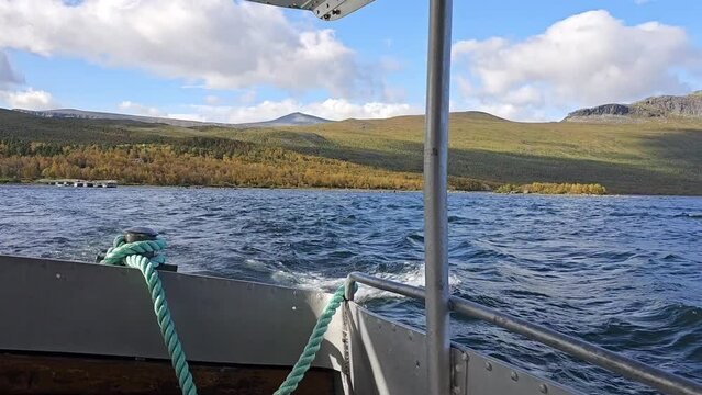 A boat swaying on the waves of Lake Langas caused by strong wind in Saltoluokta, Sweden, in the morning light and blue sky with clouds, on the Kungsleden long-distance hiking trail