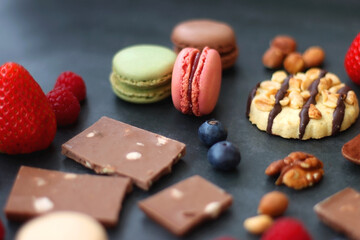 Macarons, chocolate, cookies, berries and various nuts on dark blue background. Selective focus.
