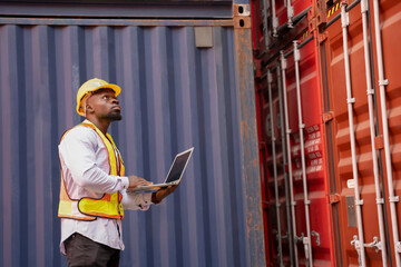 black african man wears hardhat and vest holding laptop computer checking electronic seal on container cargo,young male technician working in shipping yard,concept of container cargo shipping,industry
