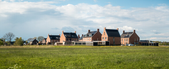 A block of newly built homes behind a field of grass in Ewijk, Gelderland, on a sunny day in spring