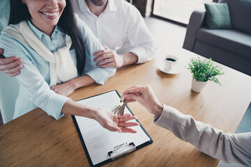 Photo of young couple meeting realtor lady arm hodl give keys desk loft interior office indoors