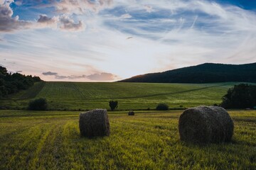 hay bales sit in a field as the sun sets behind the hills