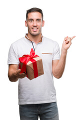 Handsome young man giving a present very happy pointing with hand and finger to the side