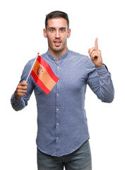 Handsome young man holding a flag of Spain surprised with an idea or question pointing finger with happy face, number one