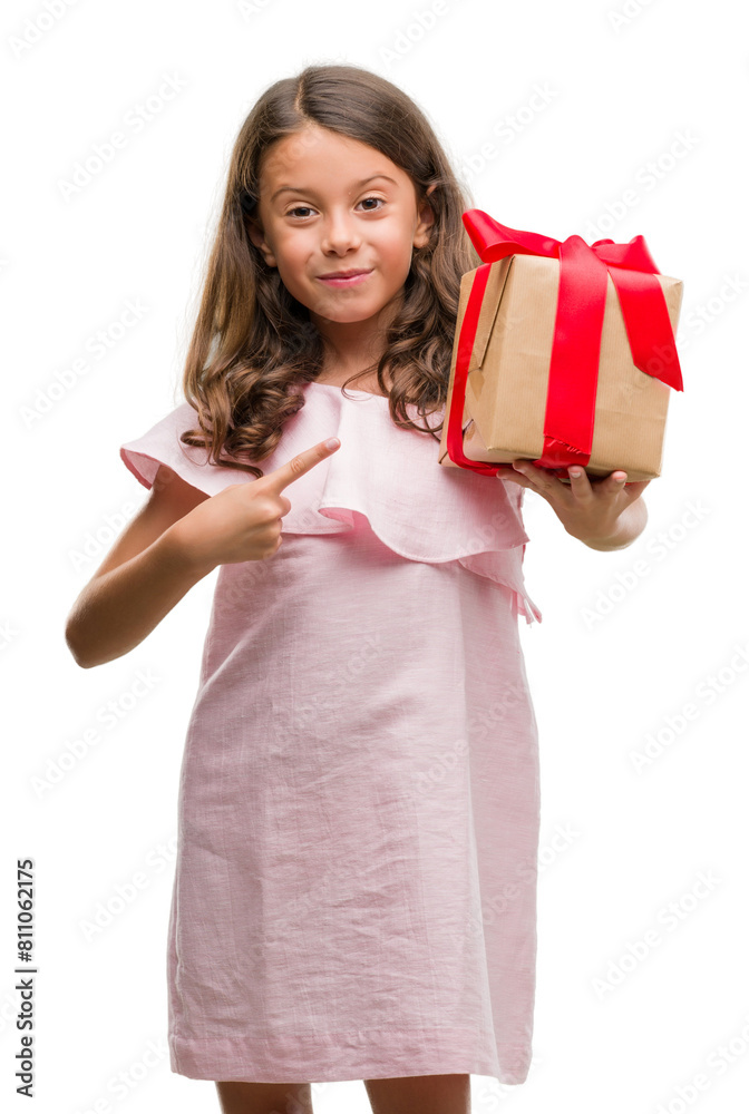 Wall mural brunette hispanic girl holding a gift very happy pointing with hand and finger