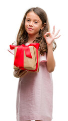 Brunette hispanic girl holding a gift doing ok sign with fingers, excellent symbol