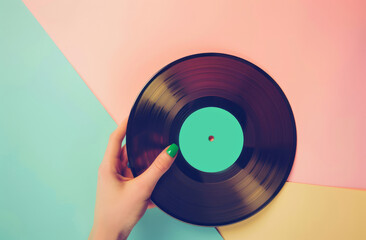 Close up of woman hand with green nail polish holding old vinyl retro record music audio on a pastel green and orange background.