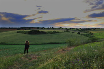 FIELD WITH TREES AND FLOWERS AT SUNSET AND A WOMAN OBSERVING THE LANDSCAPE