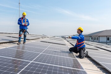 Two solar panel technicians in hardhats and safety gear inspect the installation on a commercial...