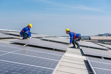 Two solar panel technicians in hard hats and safety gear install solar panels on a commercial...