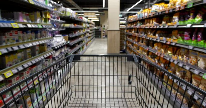 Empty shopping cart close-up rides through aisles of groceries