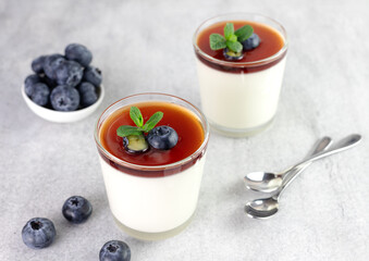 Panna cotta in glass with blueberries and sauce on gray background. Italian dessert