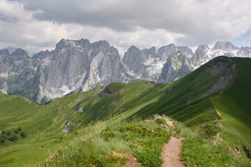 Mountain trail curving through alpine beauty. A hiker's path meanders along a green ridge,...