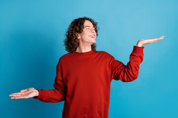 Photo of funky dreamy guy dressed red pullover showing arms scales emtpy space isolated blue color...
